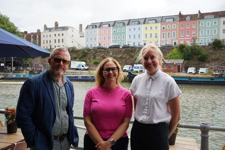 3 people smiling at a camera next to a river